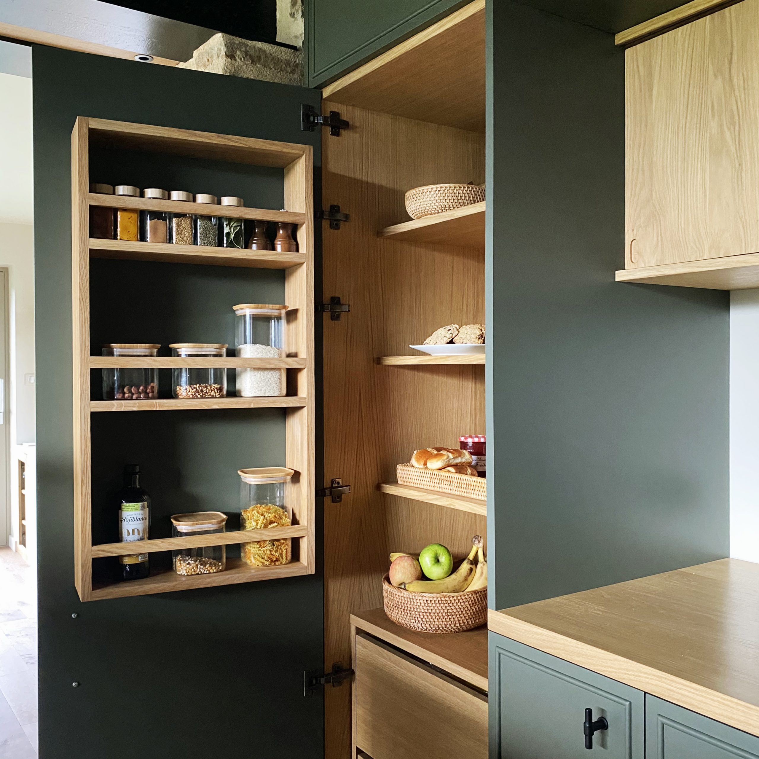 Cuisine sur mesure avec un meuble épicerie comprenant étagères et tiroirs en finition chêne et façades vert profond.